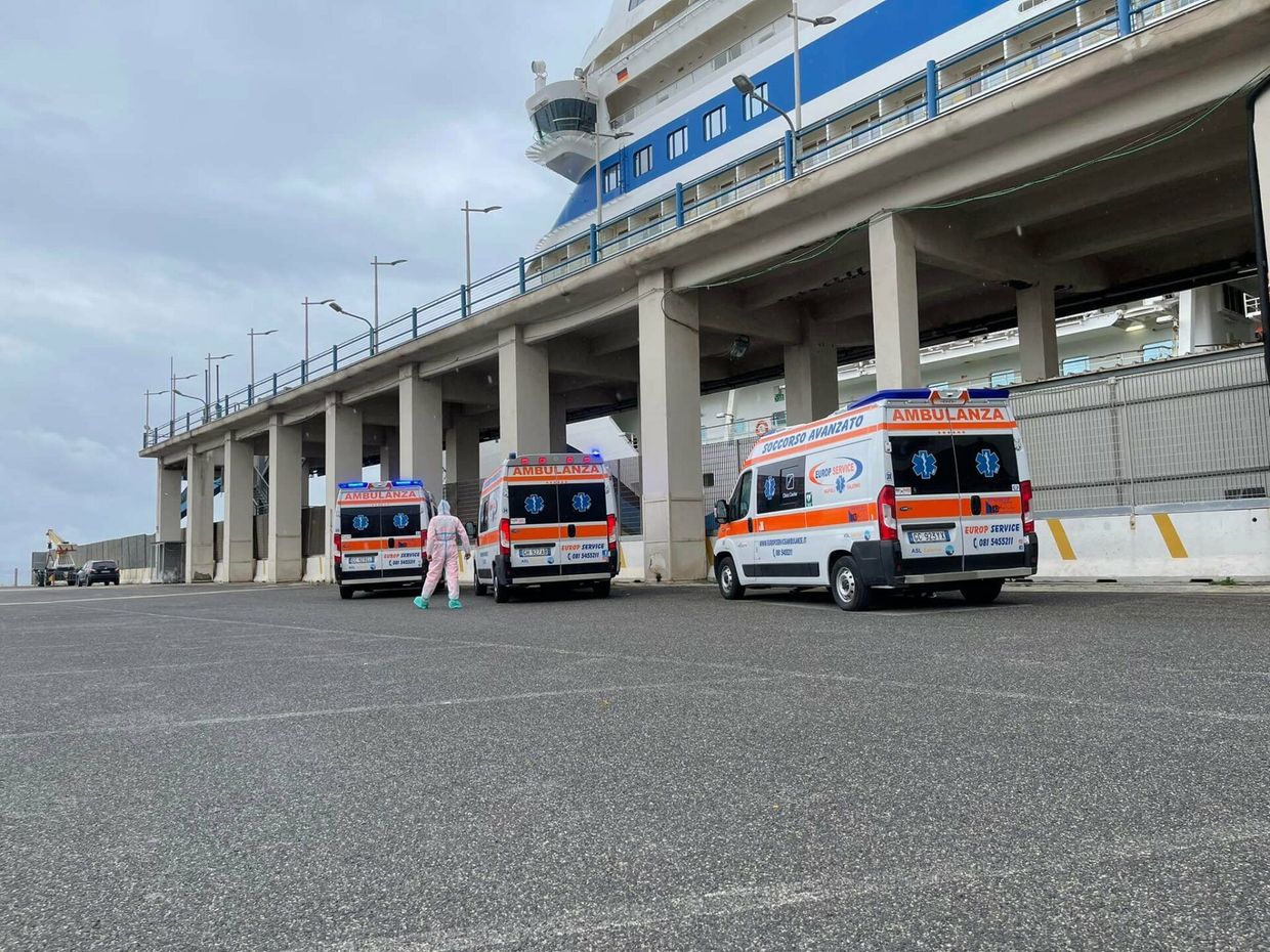 Ambulanze e paramedici all'esterno di un edificio in stile stadio su un ampio piazzale pavimentato.