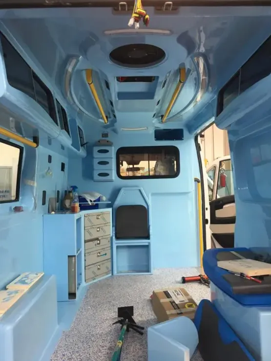 Interno di un camper blu con sedili a panca, armadietti e vani portaoggetti sopraelevati, visto dalla parte posteriore verso la parte anteriore.