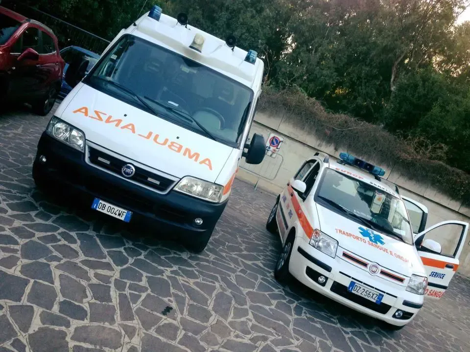 Due ambulanze bianche parcheggiate su un piazzale di pietra, una delle quali angolata verso la telecamera con scritte arancioni.