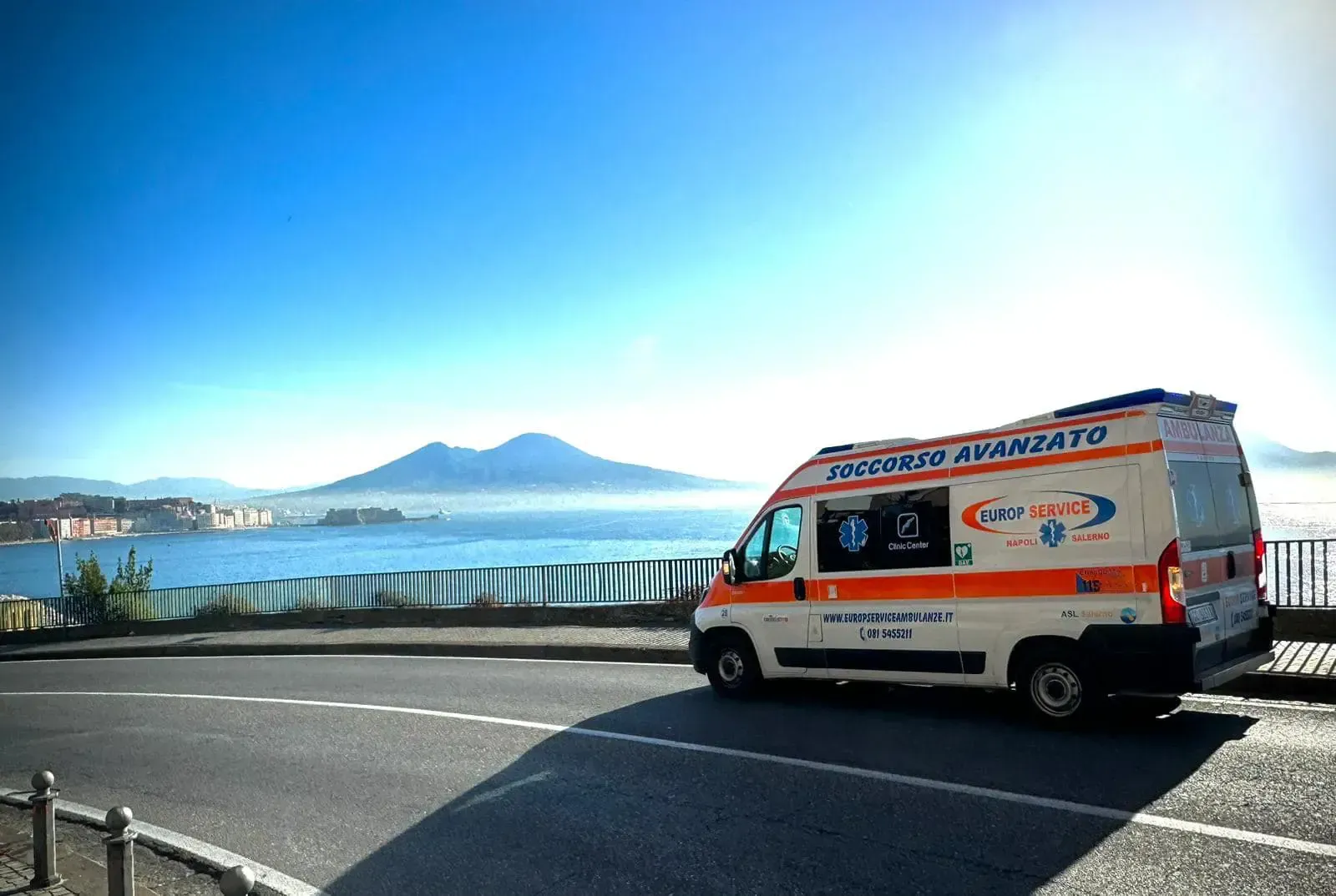 Ambulanza parcheggiata lungo una strada costiera con una montagna sullo sfondo.