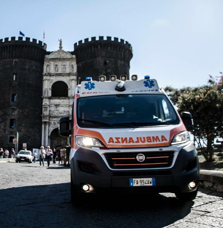 Ambulanza parcheggiata davanti a un portale storico in pietra con due torri gemelle in una piazza lastricata.