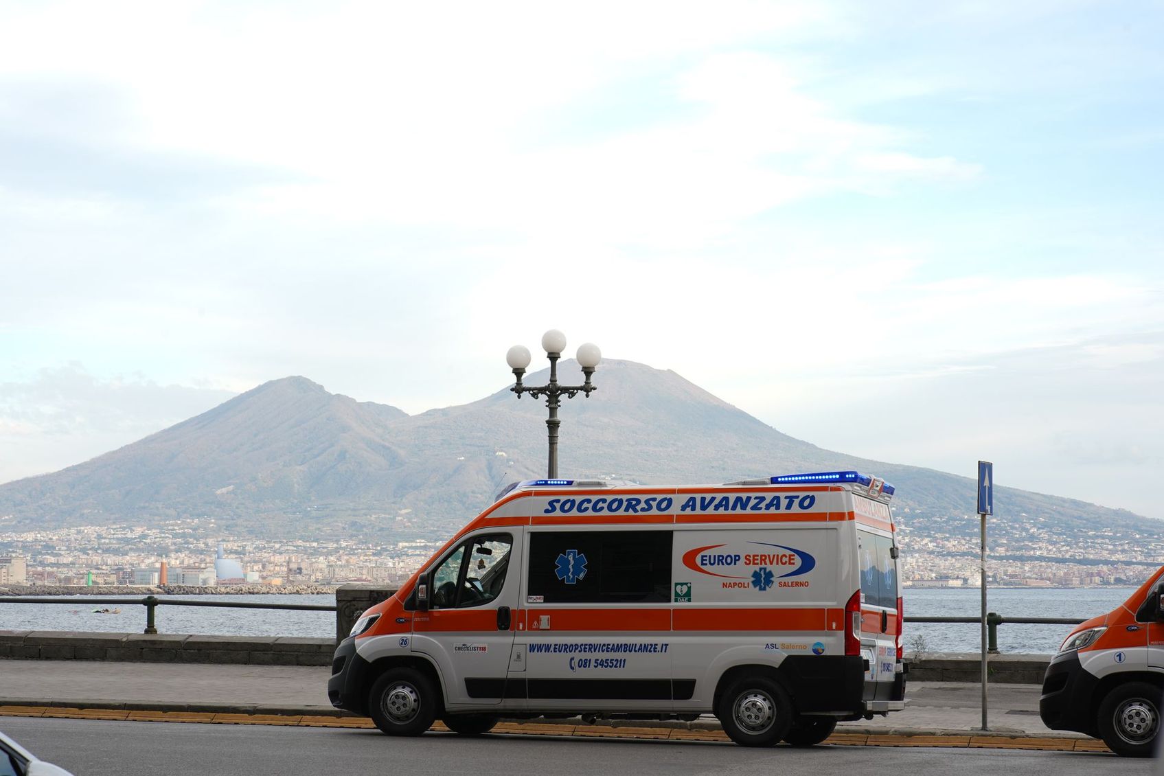 Ambulanza di emergenza parcheggiata in riva al mare con le montagne sullo sfondo.