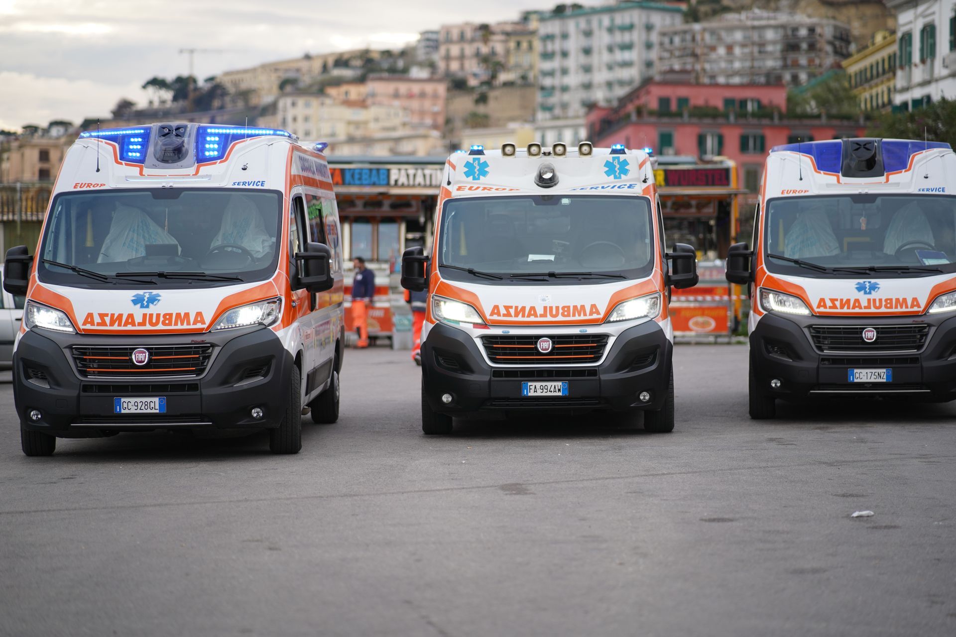 Tre ambulanze allineate su una strada cittadina con edifici sullo sfondo.