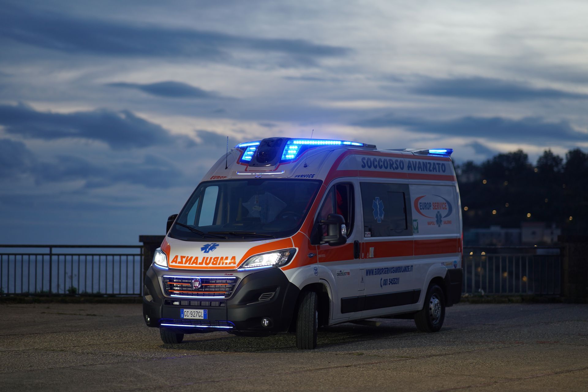 Ambulanza con luci blu lampeggianti parcheggiata sul lungomare al crepuscolo