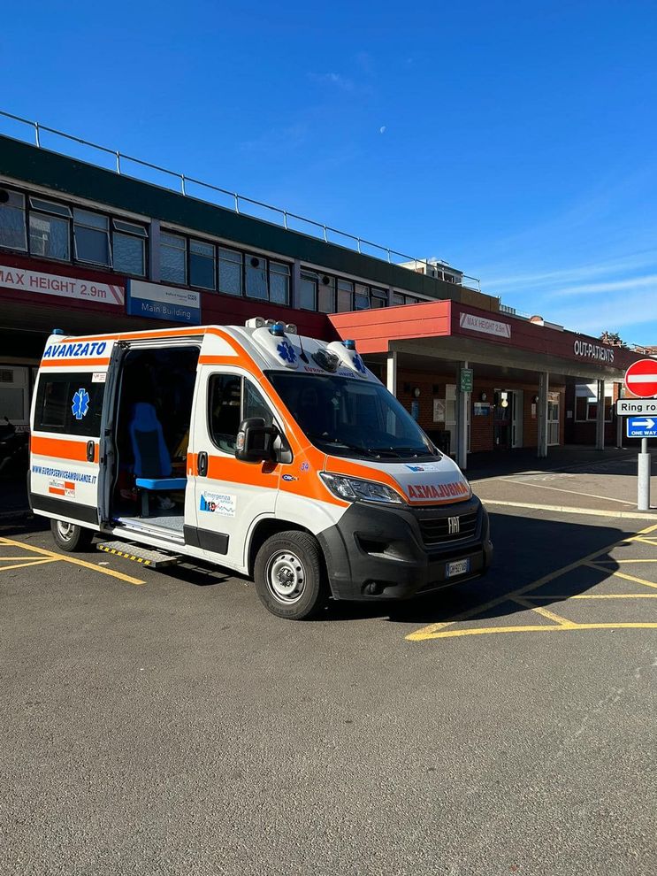 Un'ambulanza parcheggiata davanti all'ingresso di un ospedale in una giornata di sole, con le porte posteriori aperte.