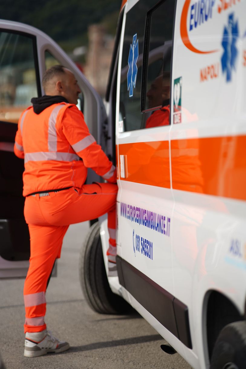 Un paramedico in uniforme arancione brillante sale su un'ambulanza dalla porta laterale.