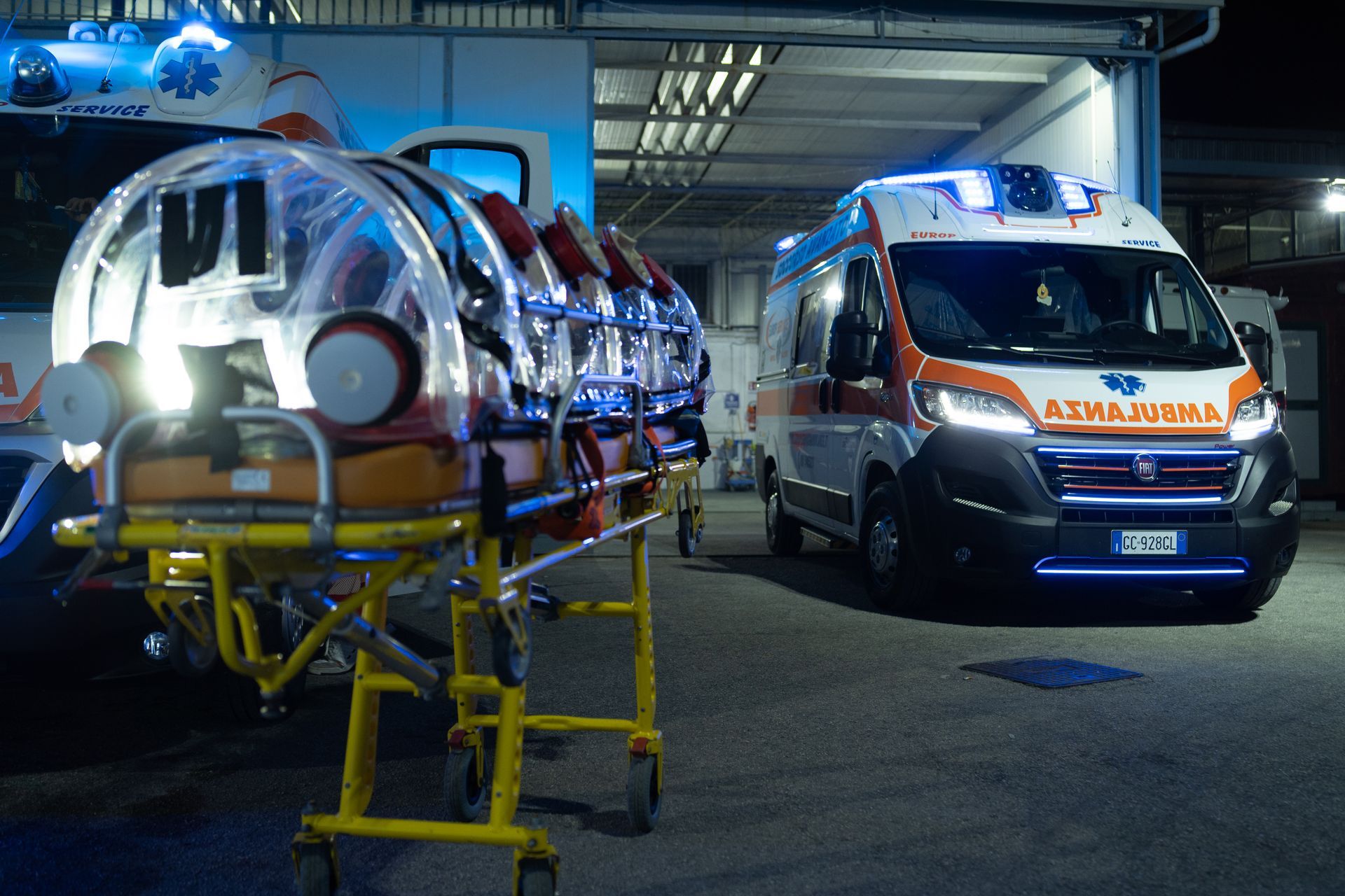 Due ambulanze in un garage, una con una barella e le luci blu lampeggianti.