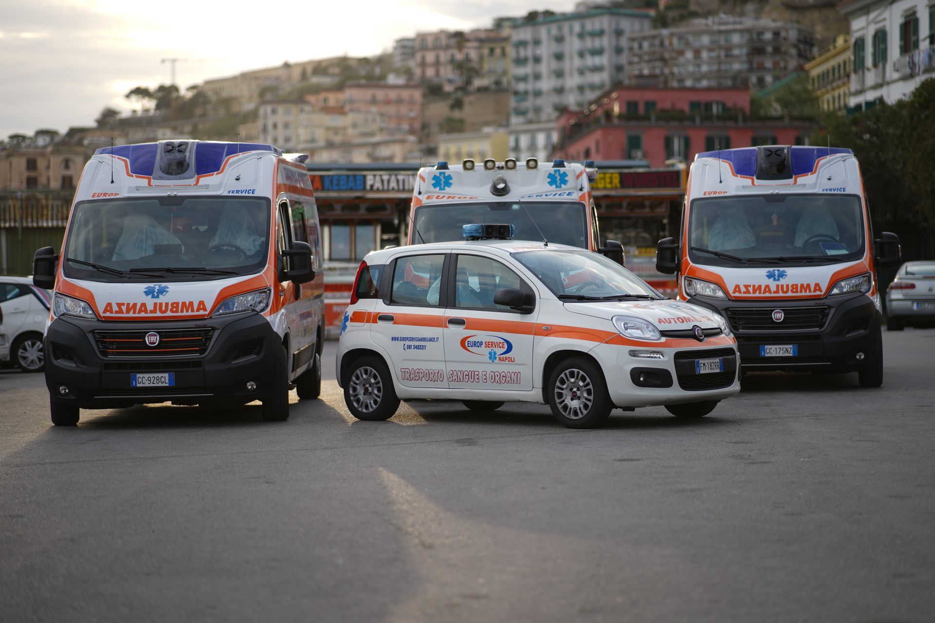 Tre ambulanze e un veicolo medico parcheggiati in una strada di fronte agli edifici.