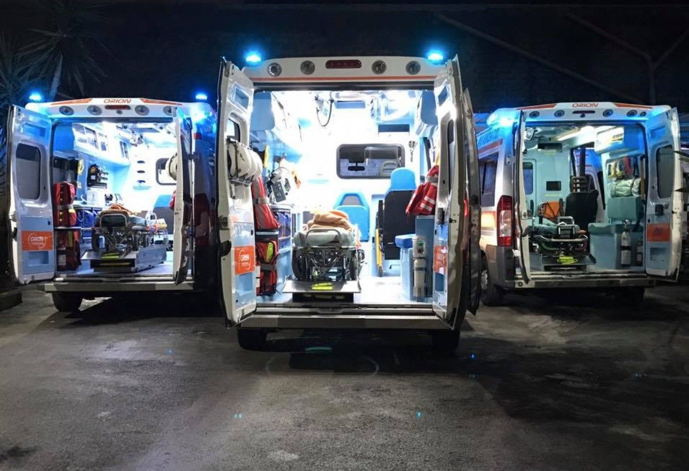 Tre ambulanze aperte illuminate di blu di notte, che lasciano intravedere le attrezzature mediche al loro interno.