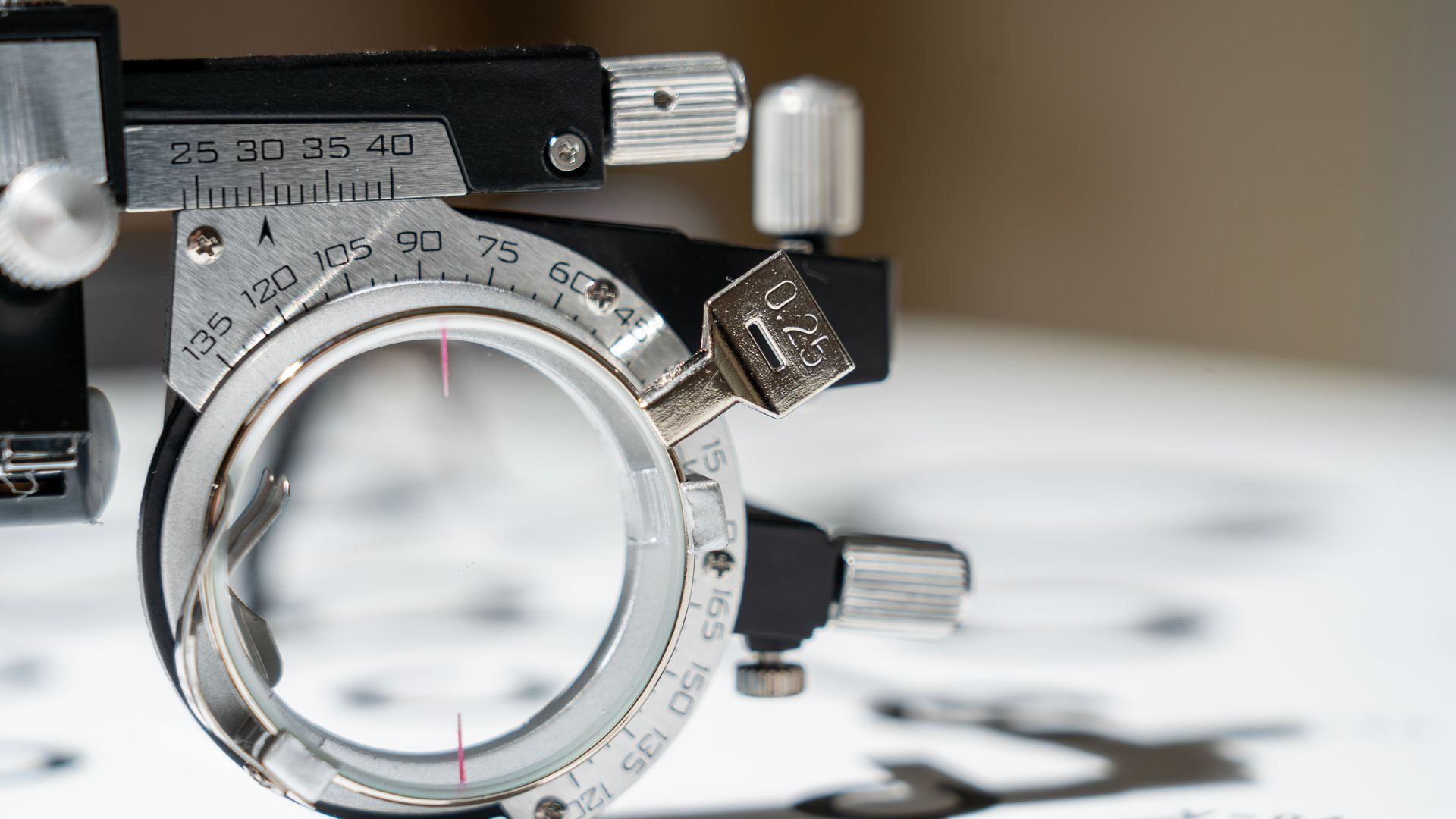 A close-up of an optometry phoropter lens dial with numbers and reflective glass.
