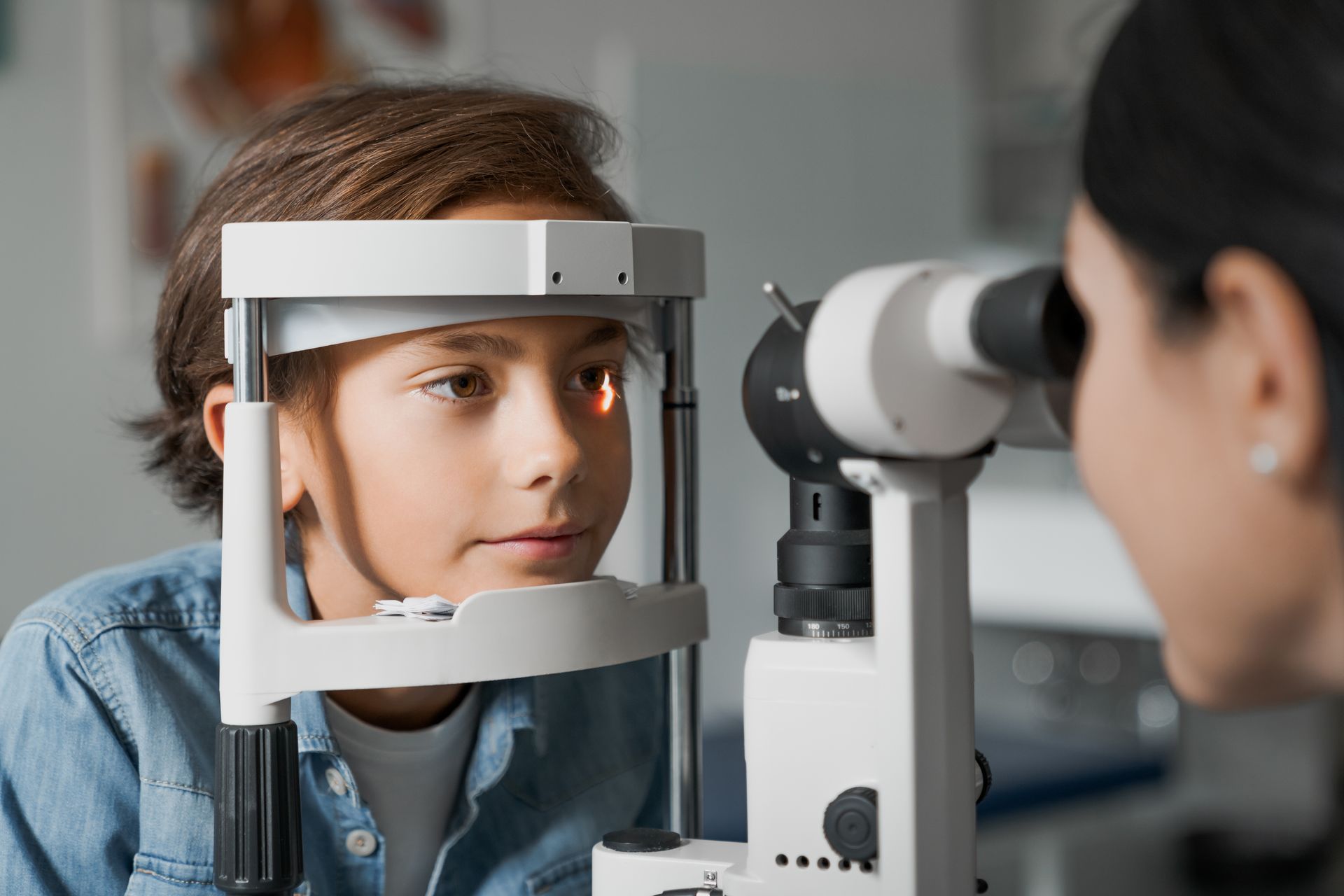 Patient in an eye exam, looking into a slit lamp while the clinician adjusts it.