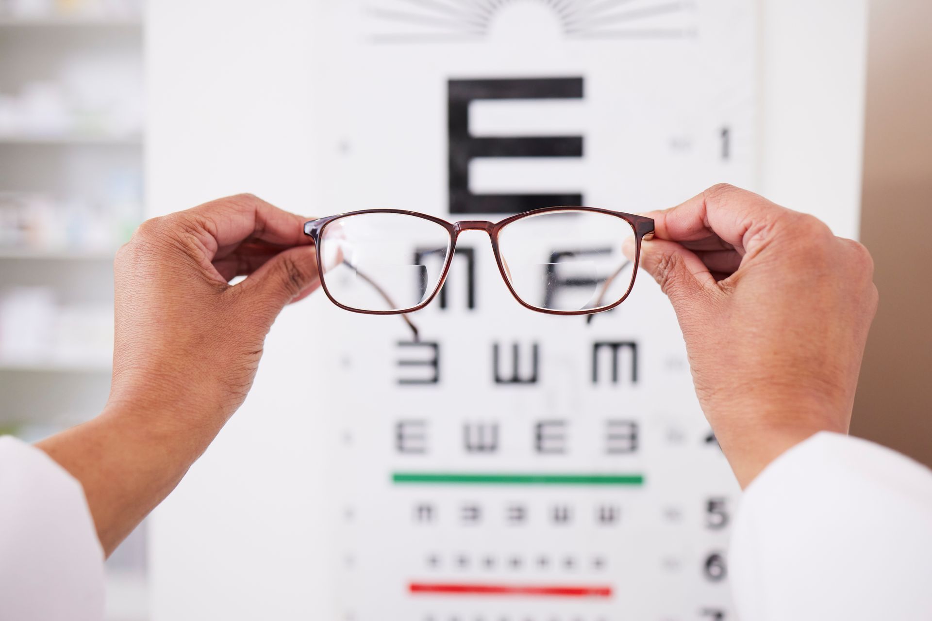 Hands holding eyeglasses in front of an eye chart during a vision test