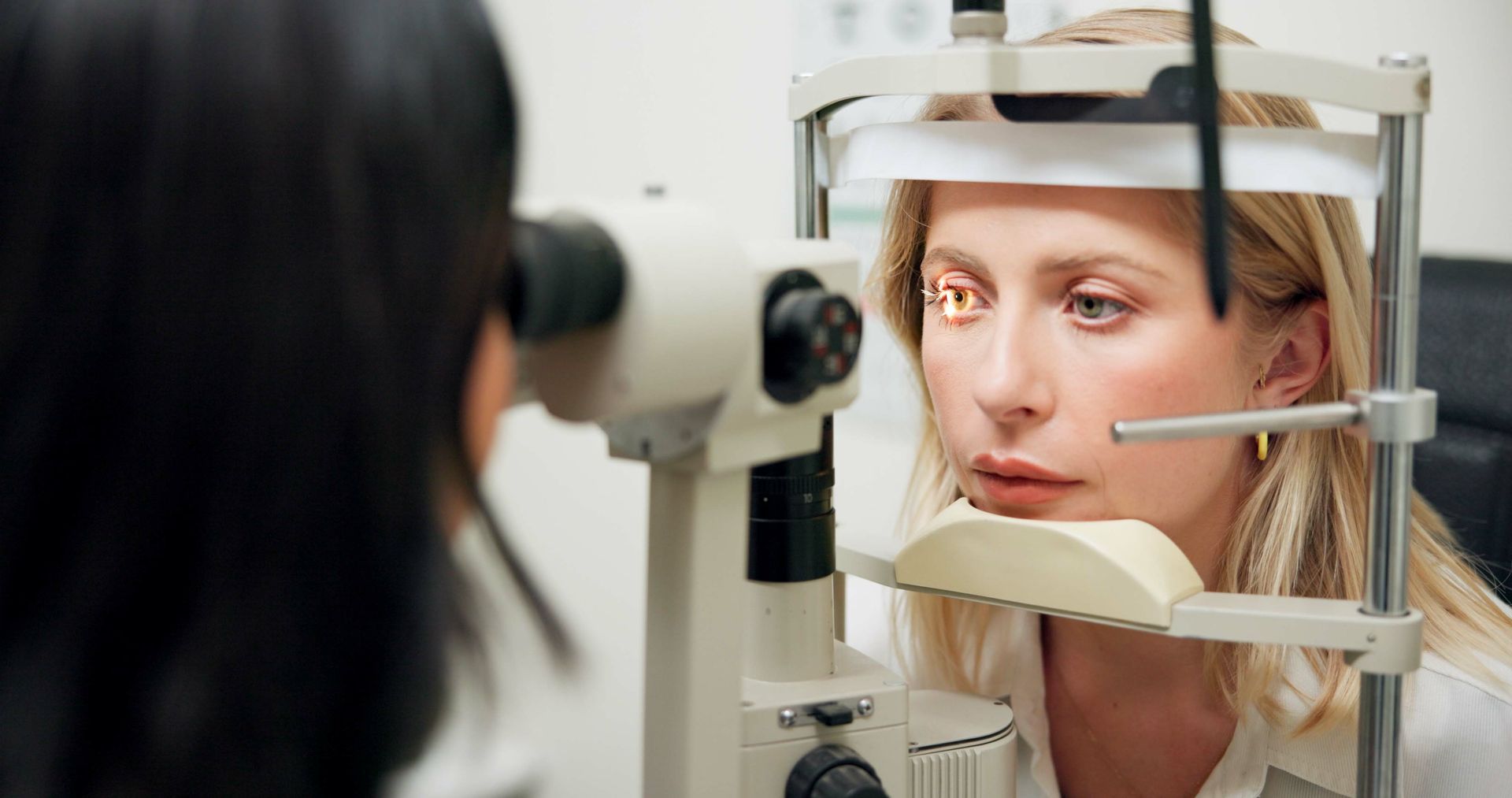 Eye exam with slit lamp as a patient looks through the instrument at an optometry clinic