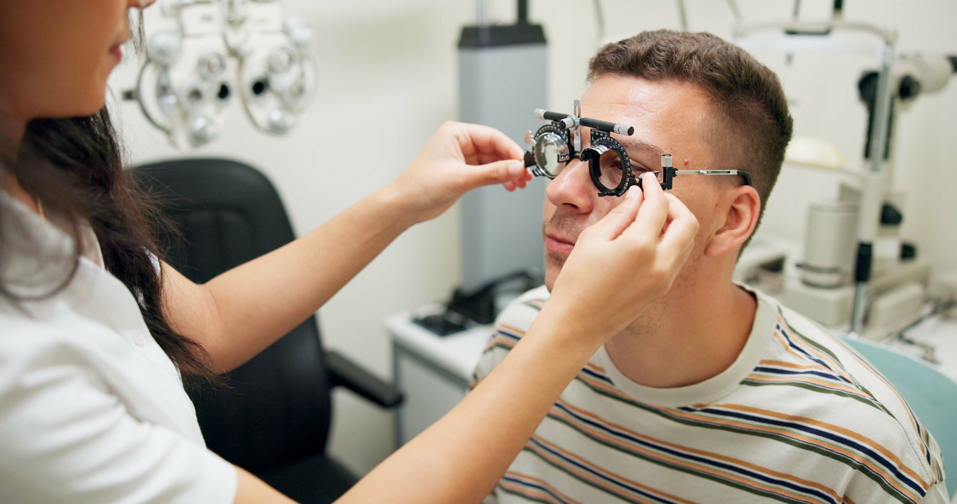 Optometrist adjusting phoropter on seated patient in eye exam room