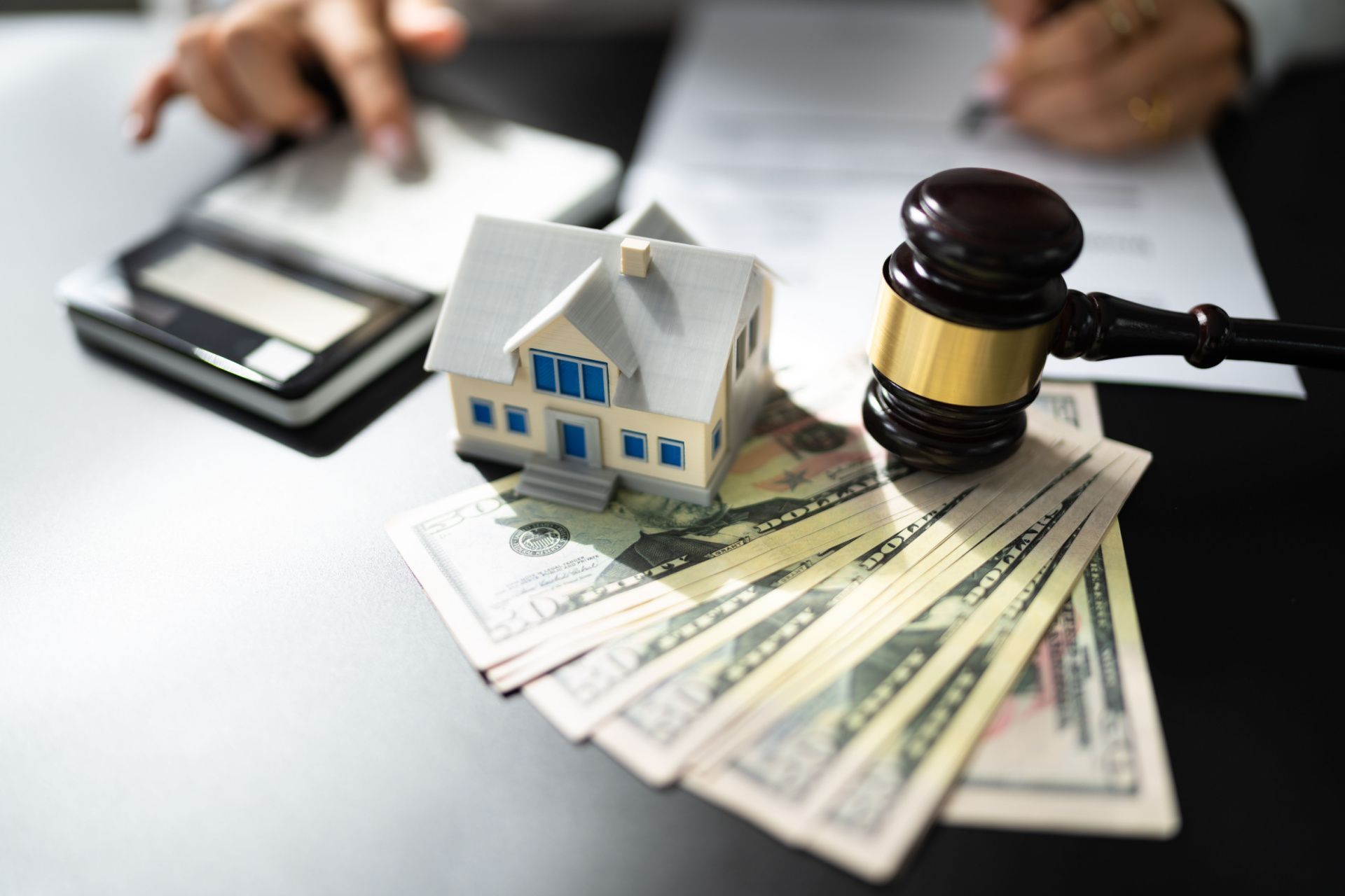 a model house is sitting on top of a pile of money next to a judge 's gavel .