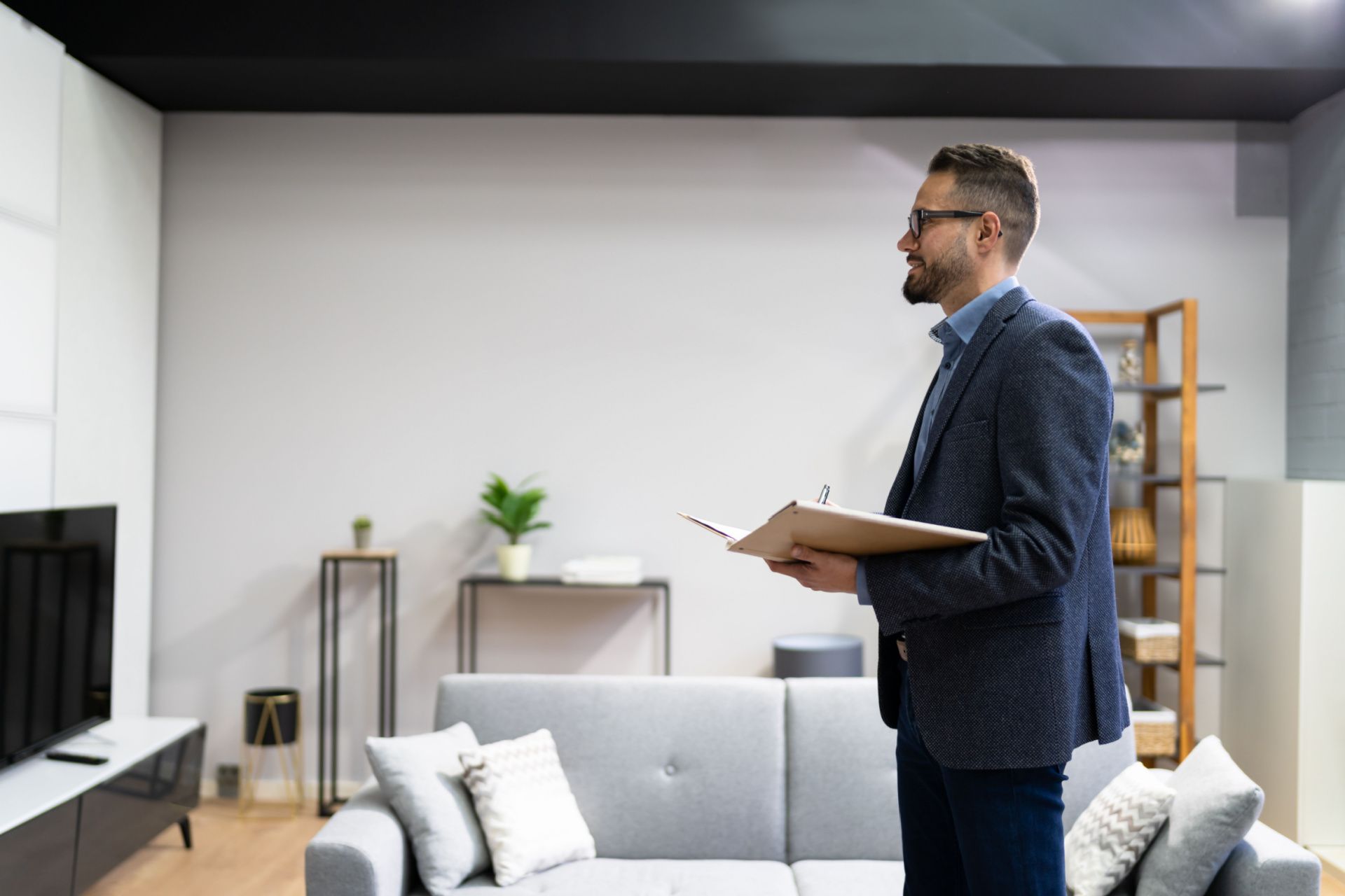 a man is standing in a living room holding a clipboard .