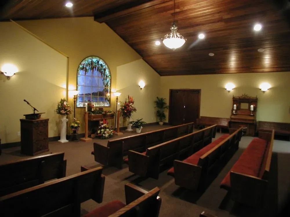 Empty church sanctuary with wooden pews, stained-glass window, altar, and warm ceiling lights