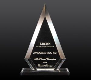 Clear glass triangular award trophy on a black base, engraved with “LBCBN” and “1996 Business of the Year.”