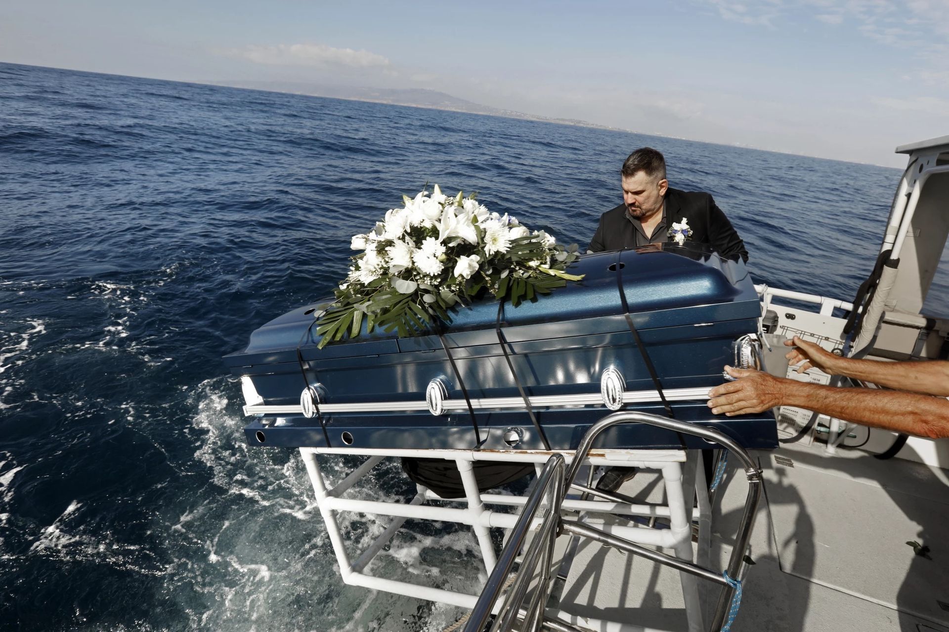 Coffin with white flowers being lowered into the sea from a boat during a burial at sea ceremony