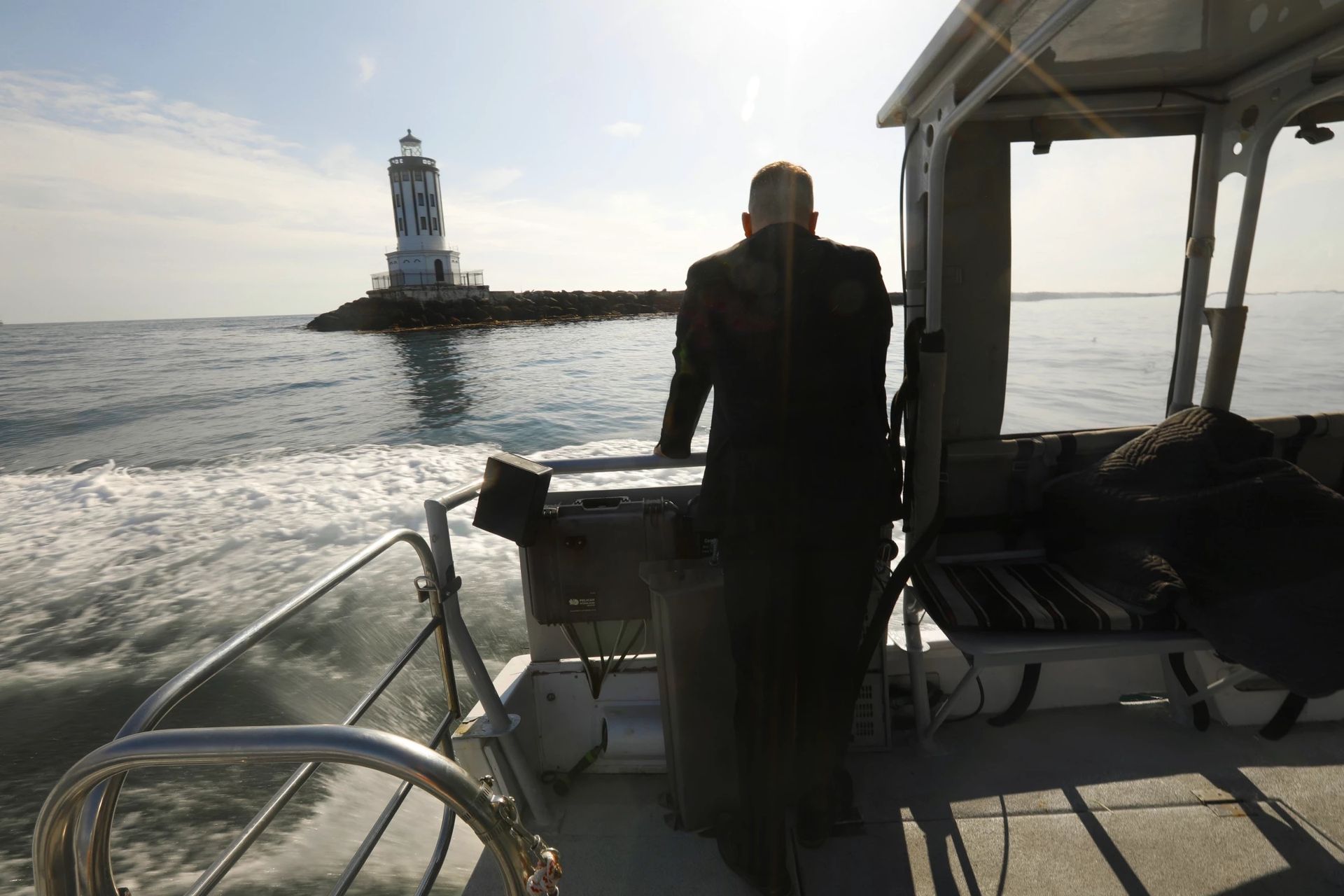 Person on a boat facing a lighthouse across calm water at sunset