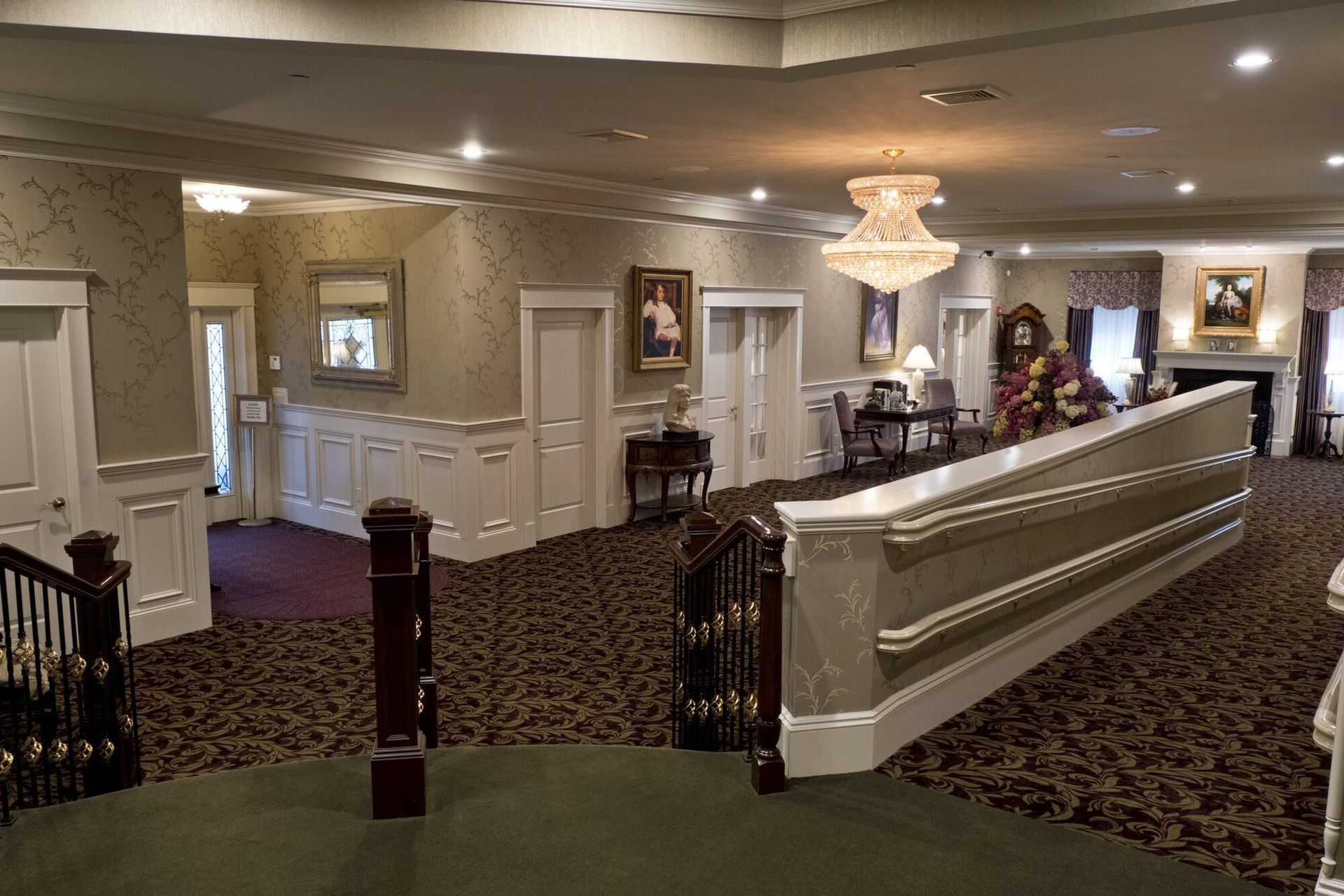 Interior of a funeral home with staircase, chandelier, artwork, and various decorative elements.