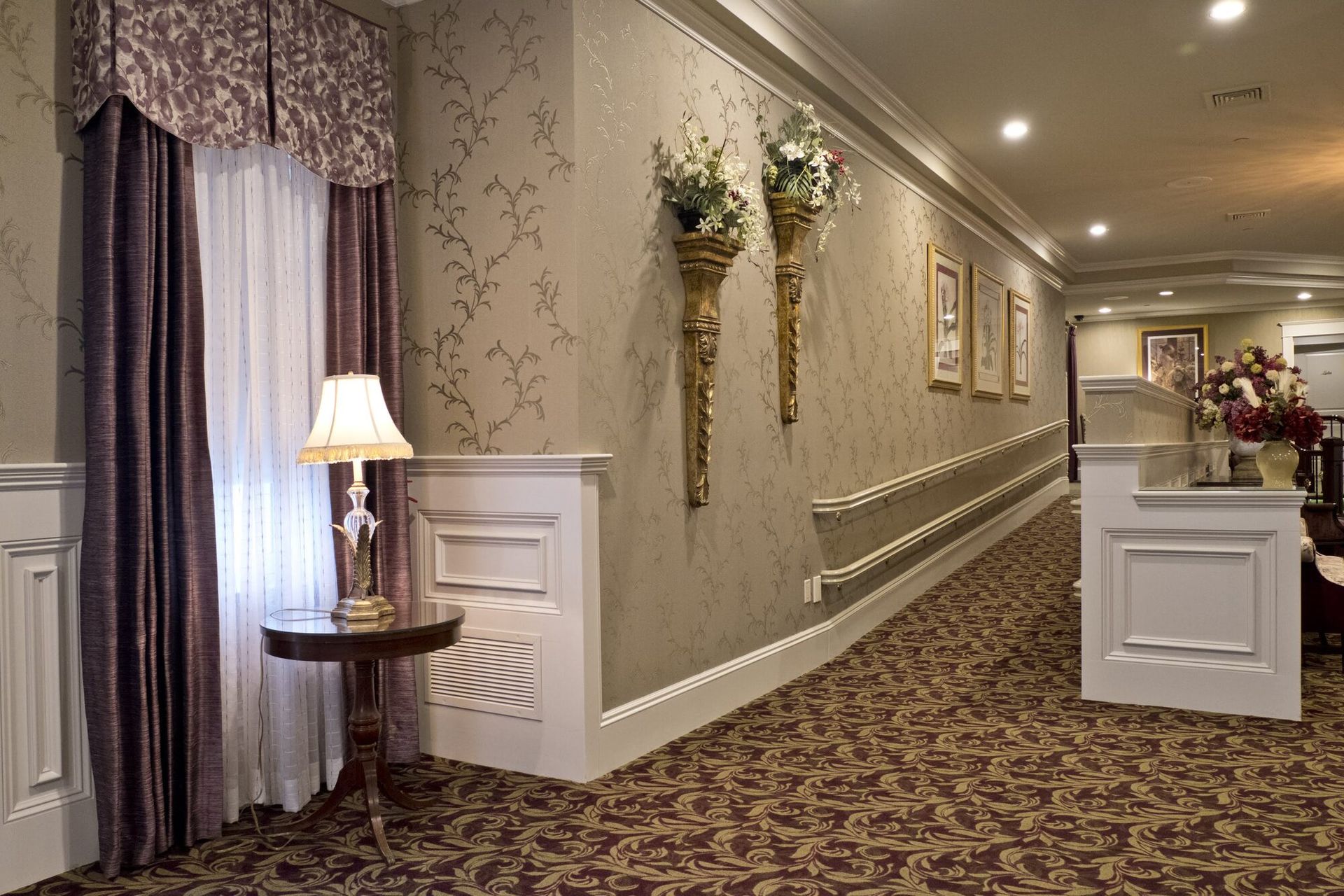 Hallway with patterned wallpaper, framed artwork, and decorative flower arrangements.