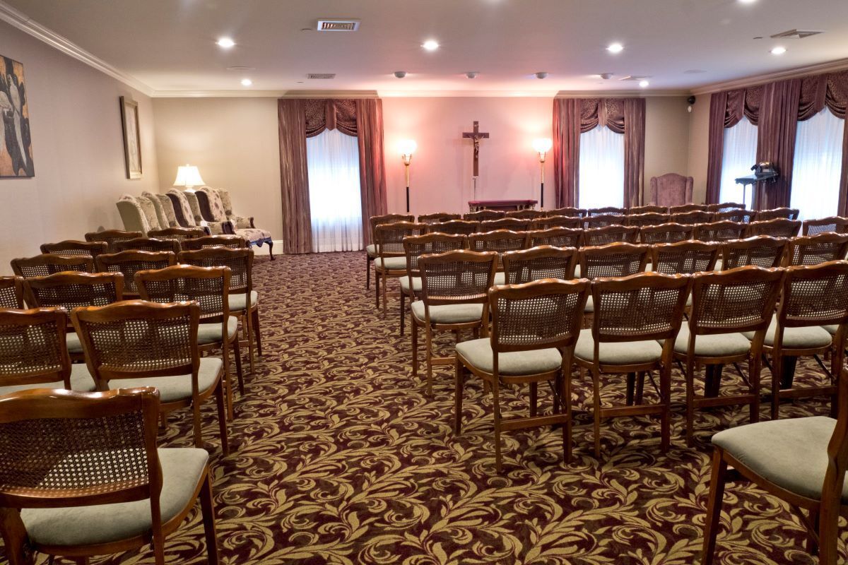 Funeral home chapel with rows of chairs facing an altar with a cross. Carpet and curtains.