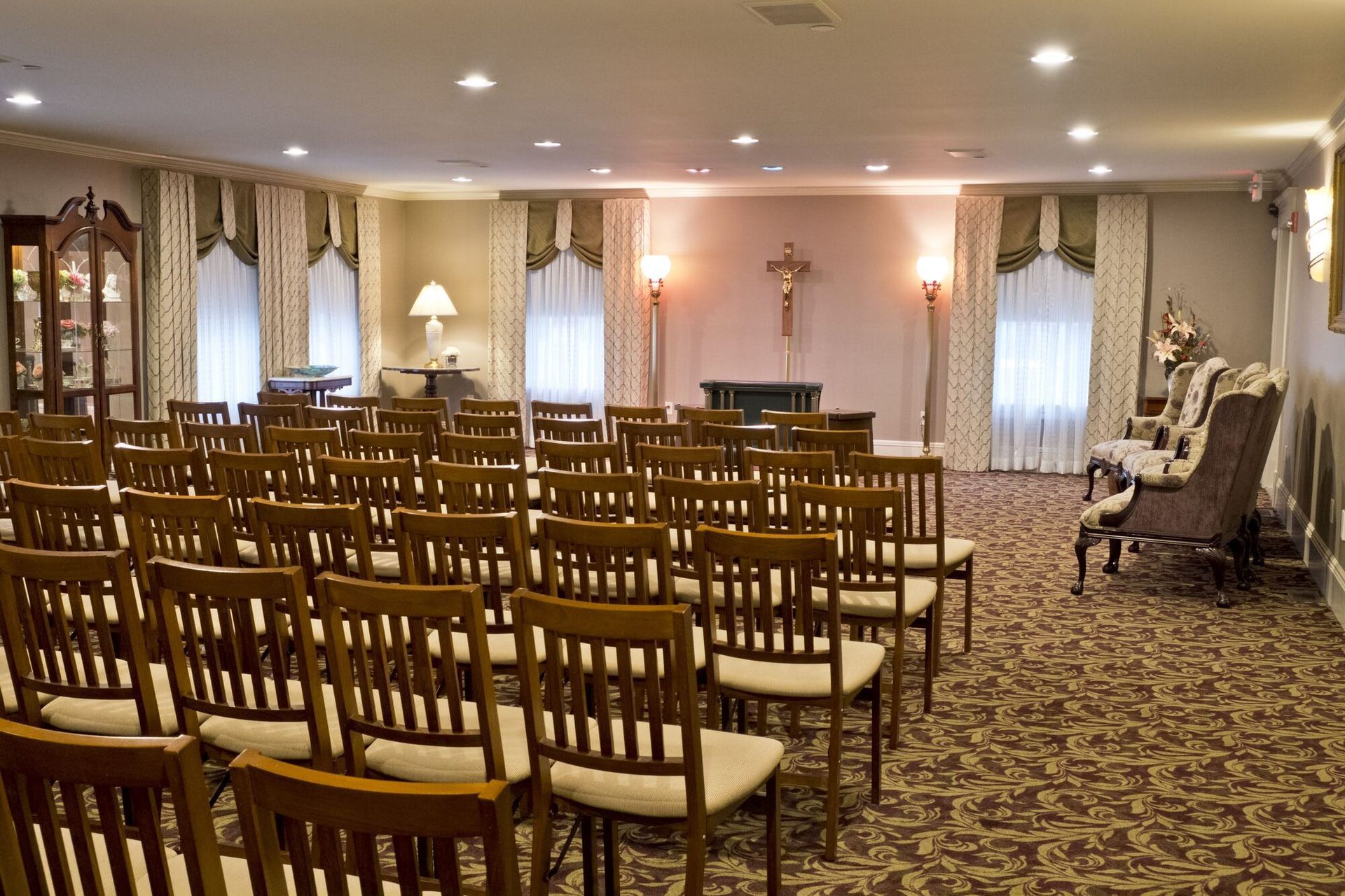 Rows of chairs face a small stage in a funeral home chapel, ornate decor.