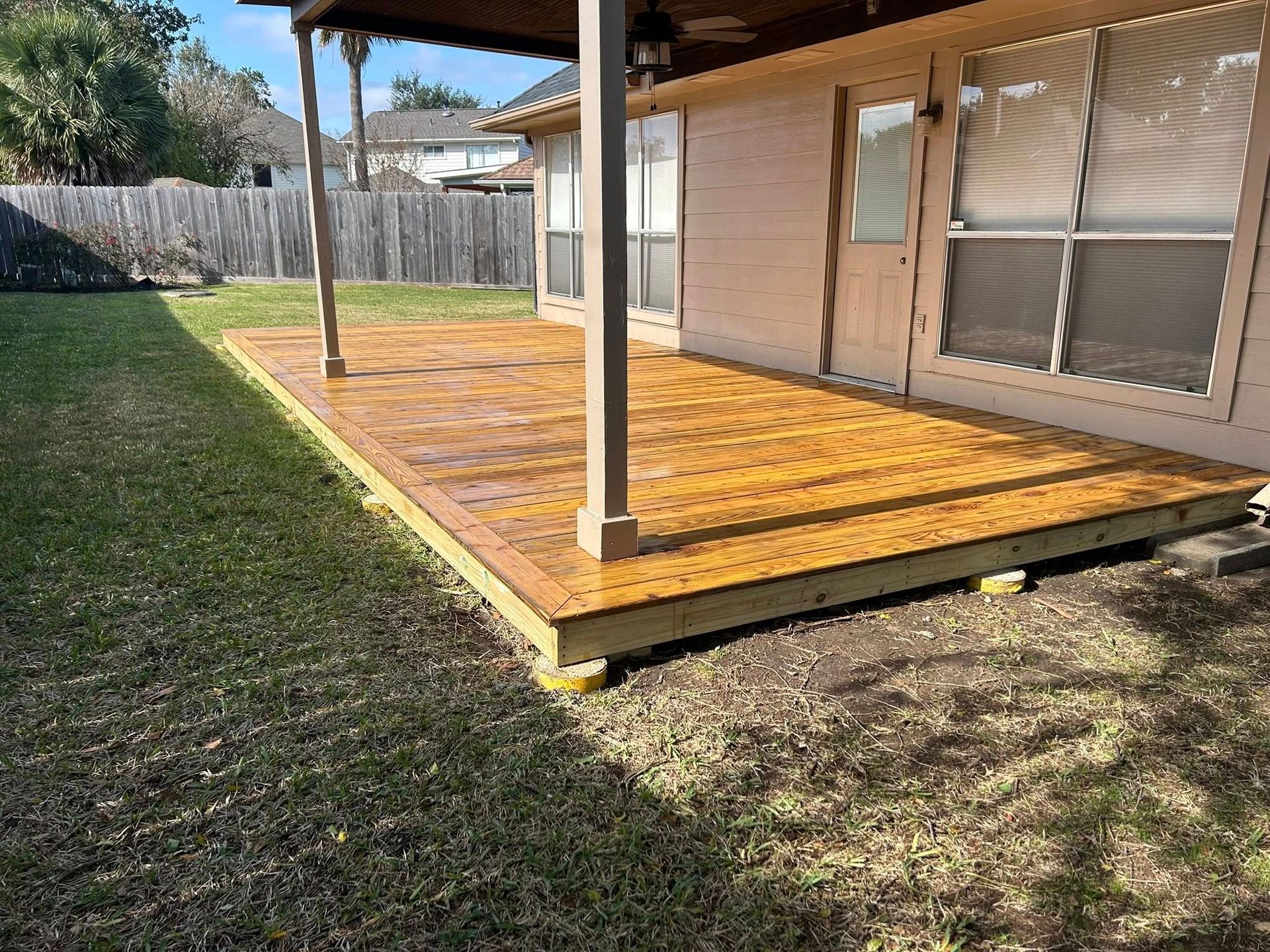 Back patio with wooden deck and covered roof beside a house, overlooking a grassy yard