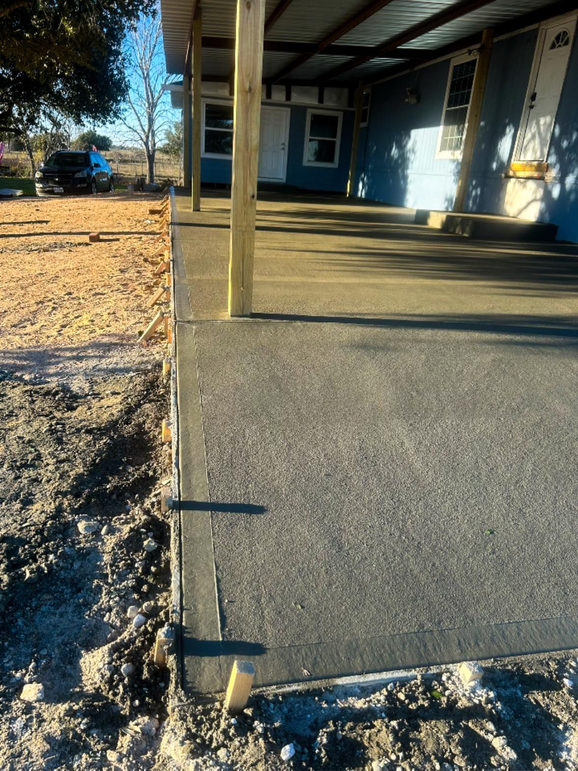 Covered porch with a blue house, concrete slab, and a gravel yard beside it.