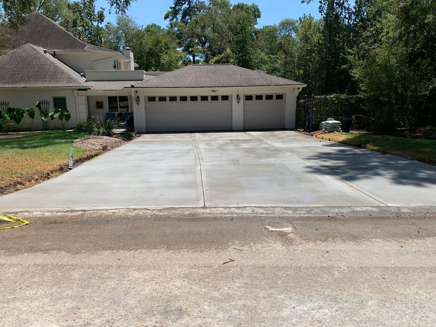 Concrete driveway leading to a two-car garage on a suburban house, with trees and blue sky.