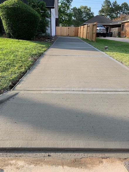 Concrete driveway leading to a wooden gate beside a grassy yard and house exterior