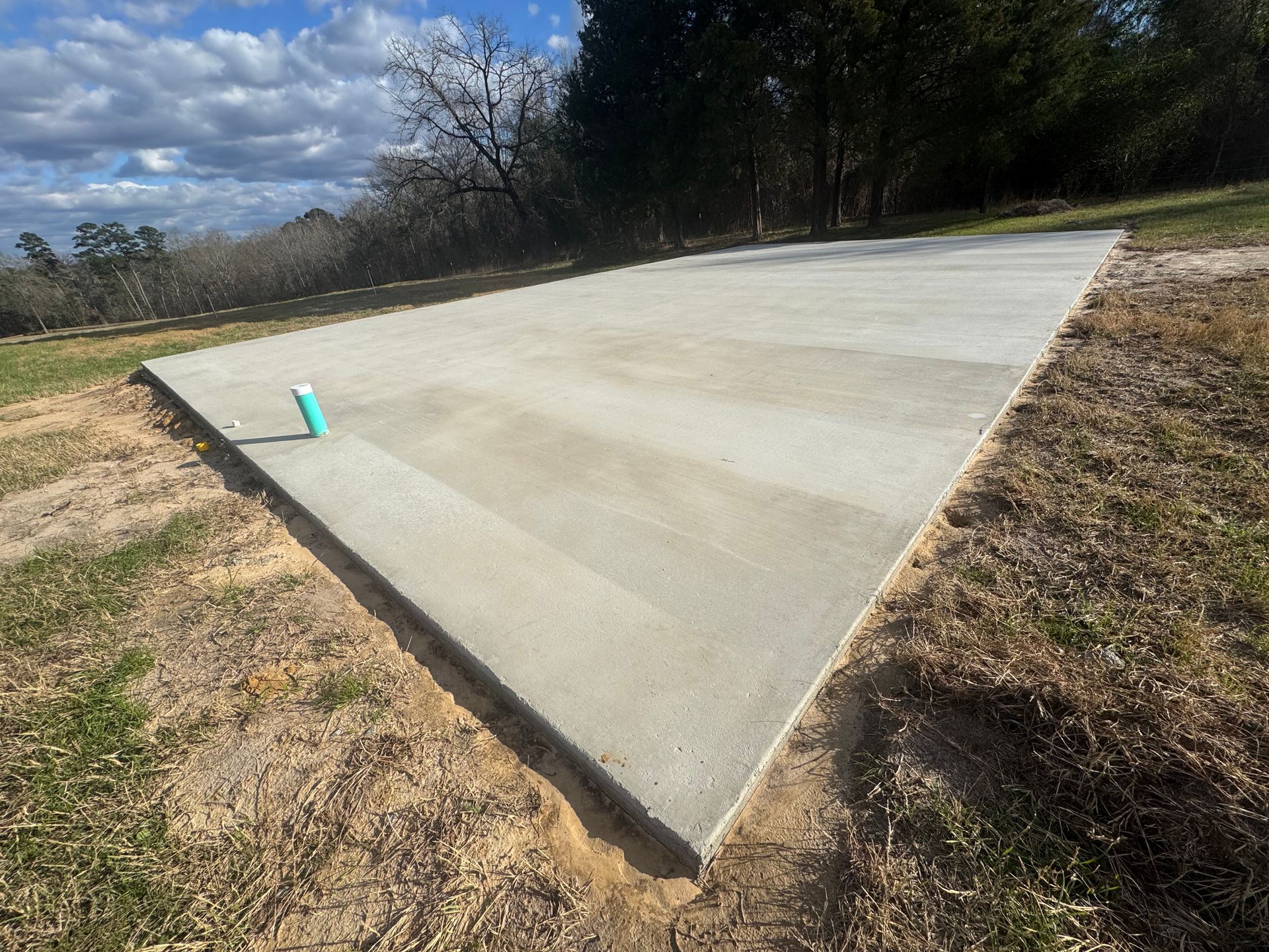 Concrete slab foundation in a grassy lot under a partly cloudy sky