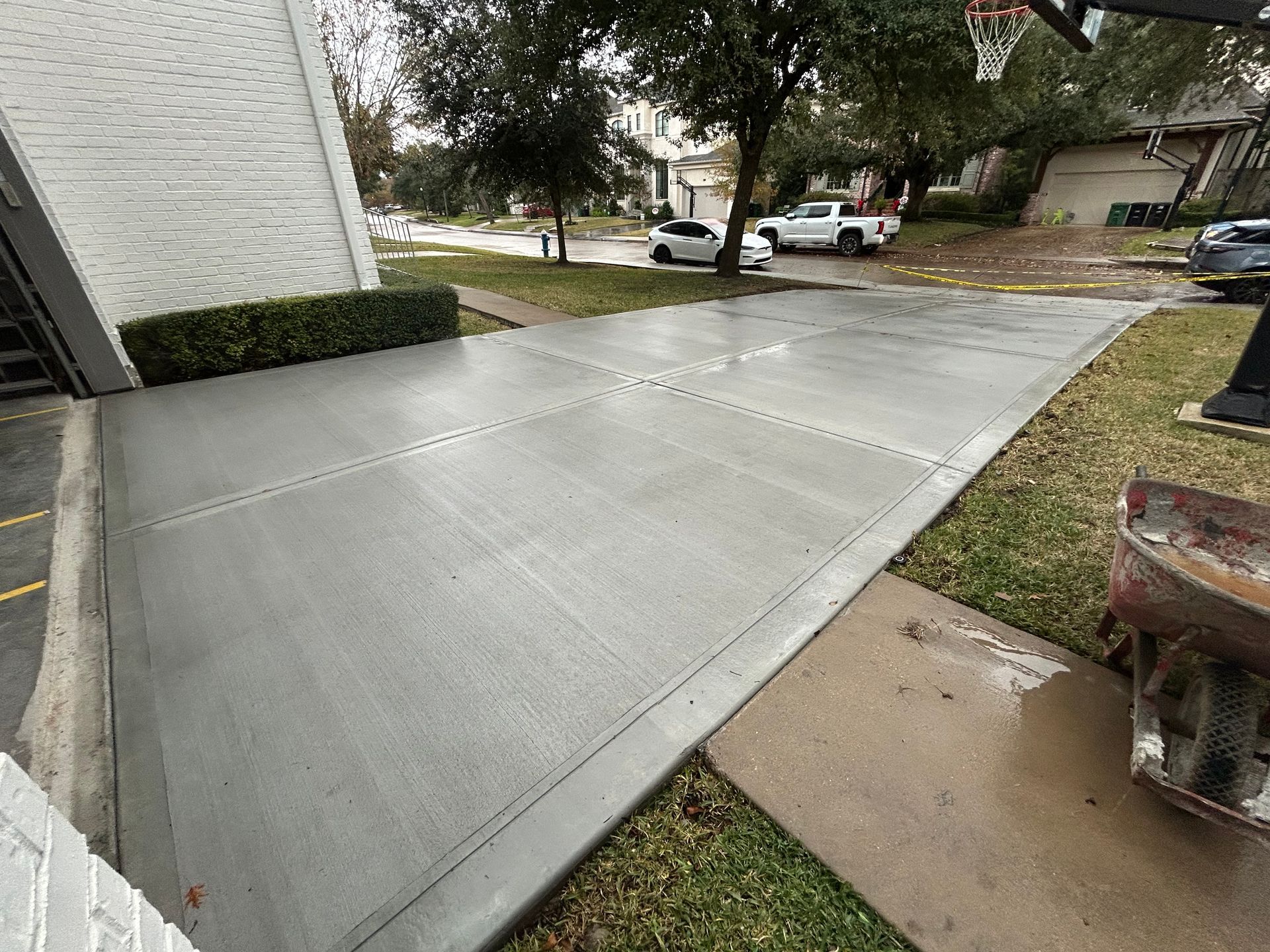 Fresh concrete driveway with expansion joints beside a white building, near a grassy street corner.