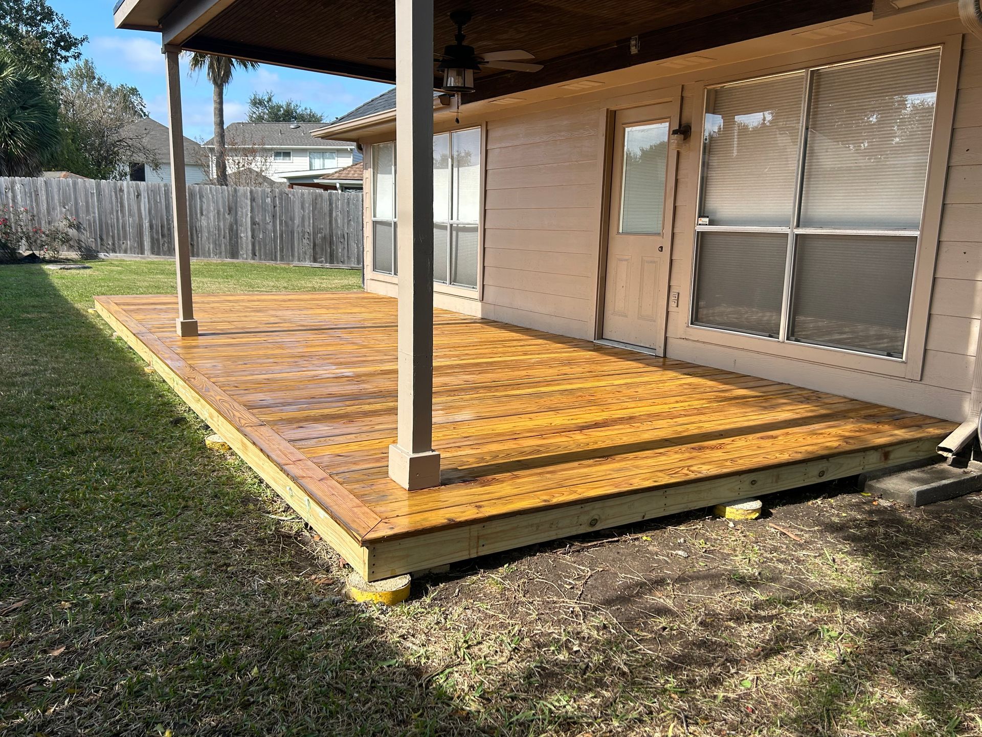 Backyard wooden deck with covered patio and support posts beside a house