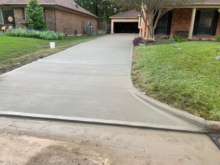 Concrete driveway leading to a brick house with a garage and a grassy lawn.
