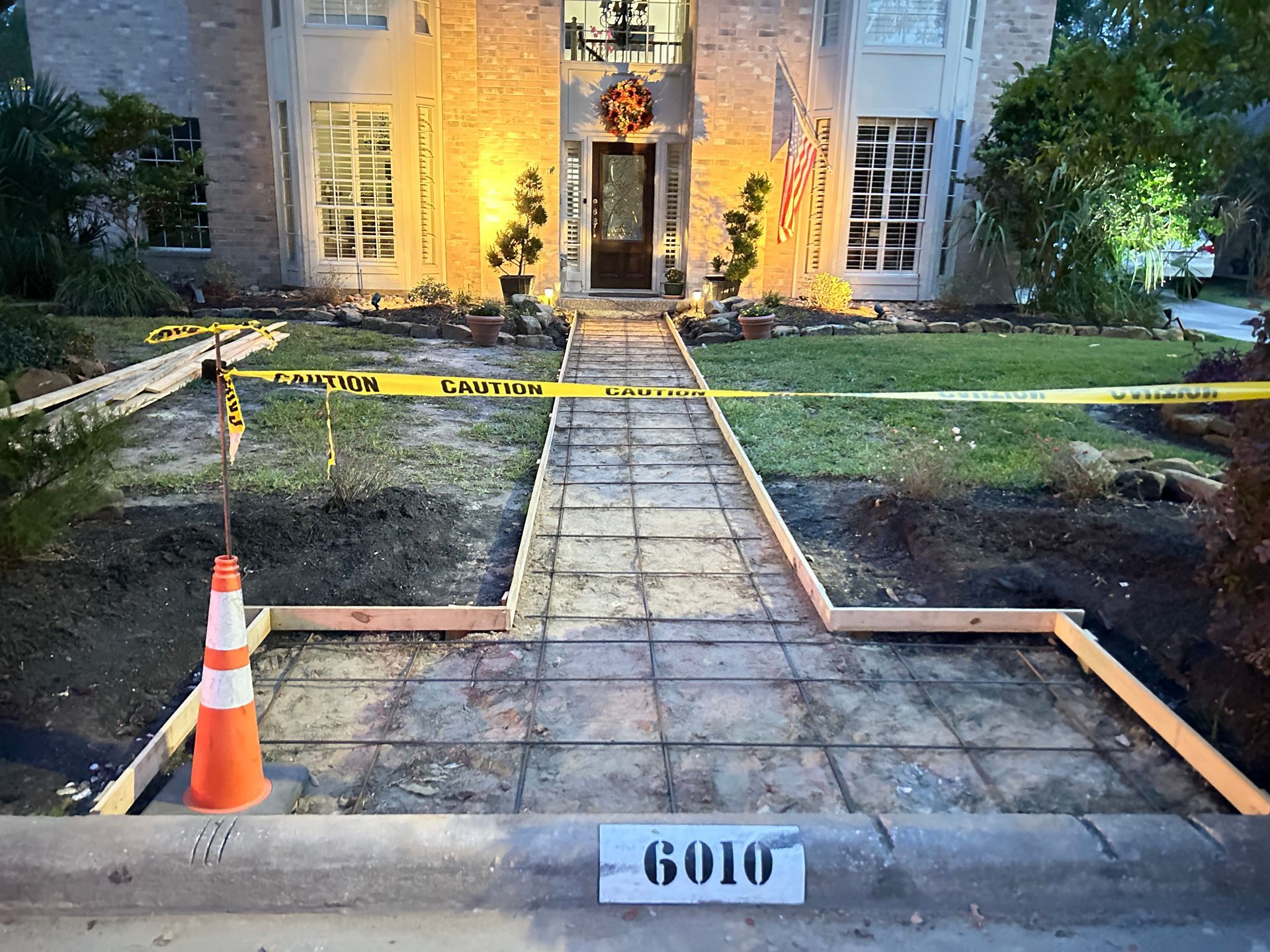 Front walkway under repair at a house, with caution tape, orange cone, and house number 6010.