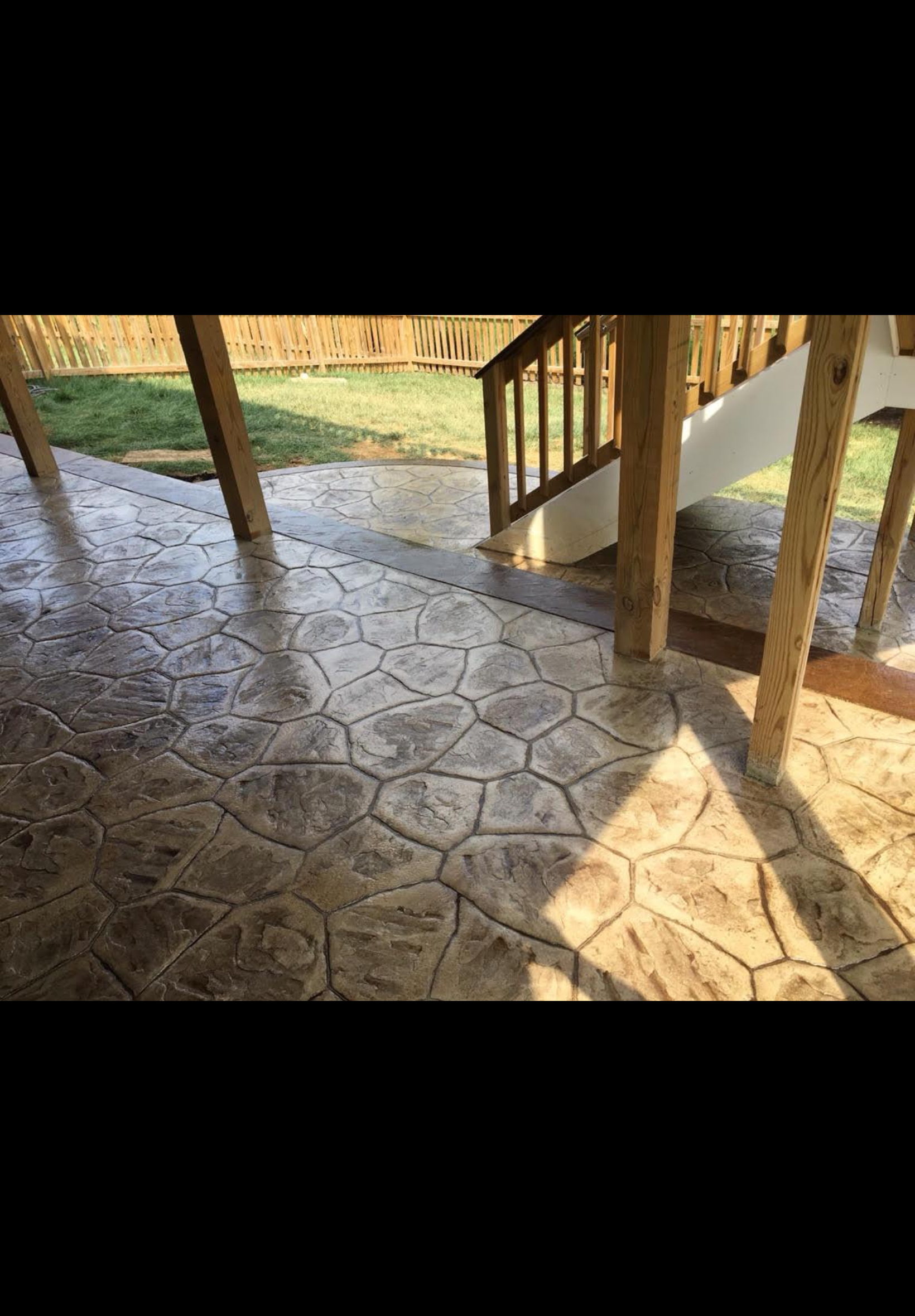 Covered stone patio with wooden posts and steps, sunlight casting shadows across the floor