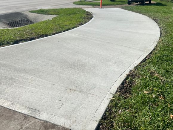 Curved concrete sidewalk beside grass and a parking lot curb