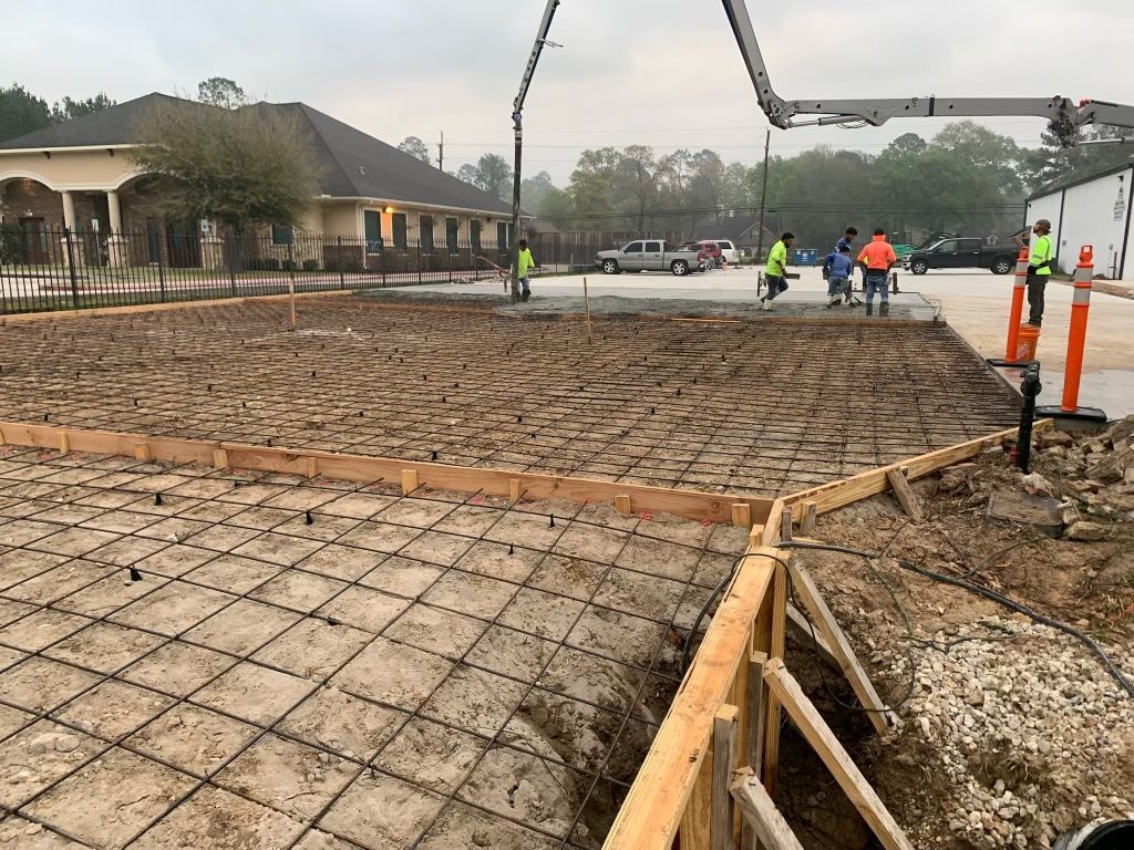 Concrete foundation work with rebar grid and workers at a construction site, next to a house on a cloudy day
