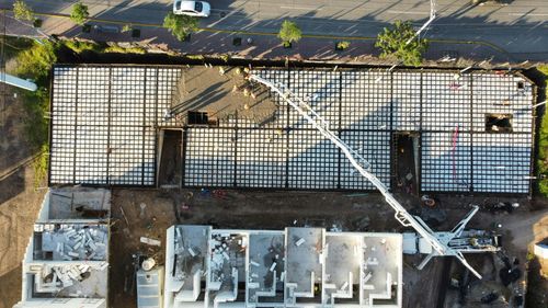 Aerial view of a building roof with solar panels, a white crane arm, and parked vehicles below.