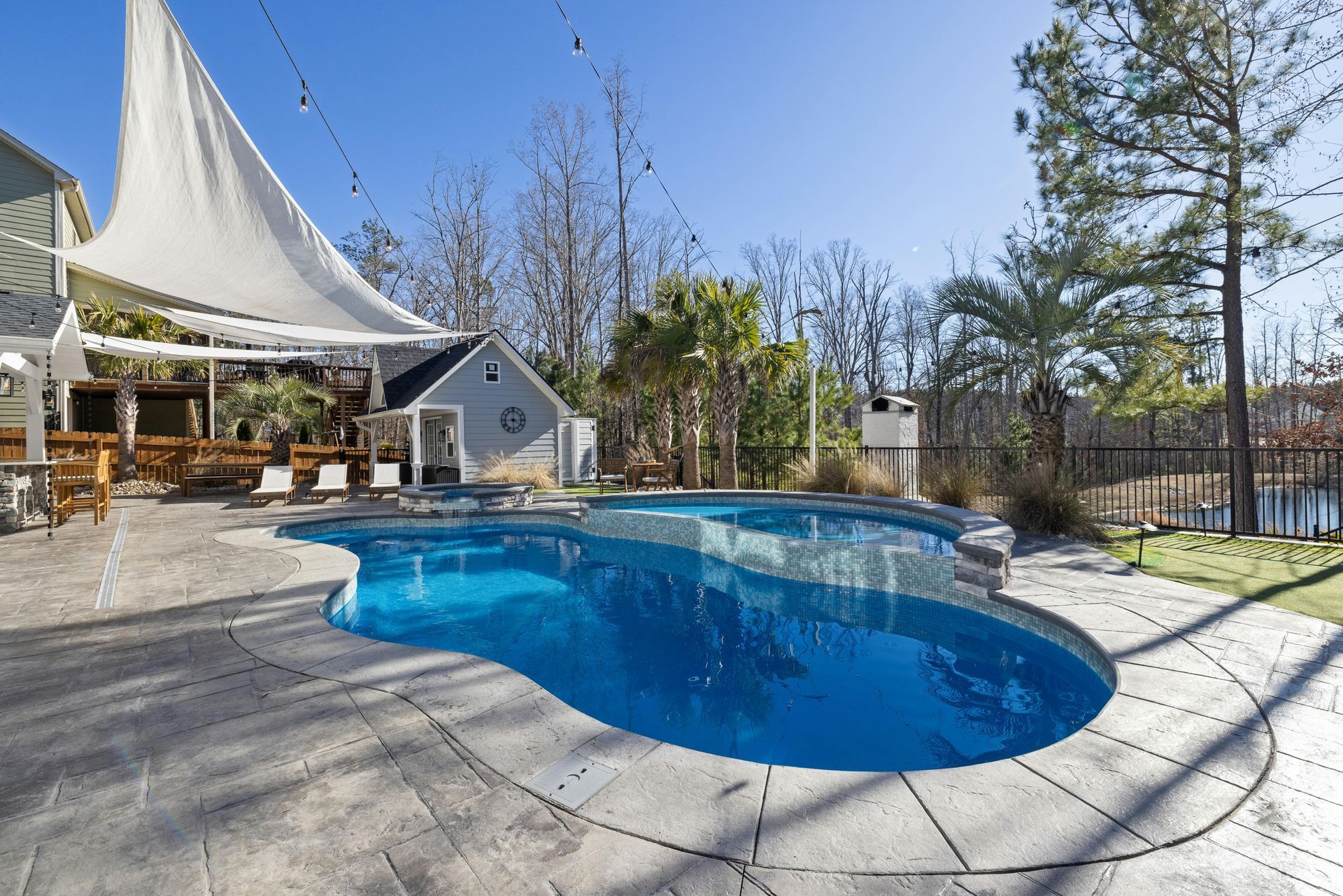 Backyard pool with blue water, stone patio, and shaded seating under a white canopy