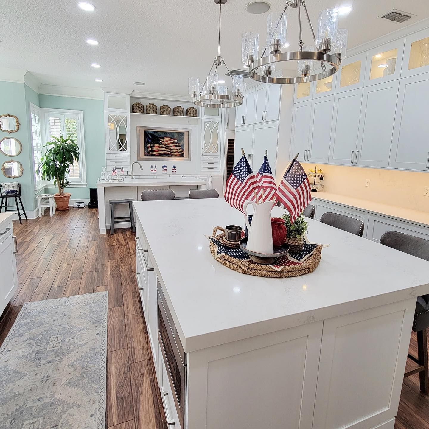 Spacious, bright kitchen with a large island and American flags. White cabinets, wood floors, and decorative chandelier.