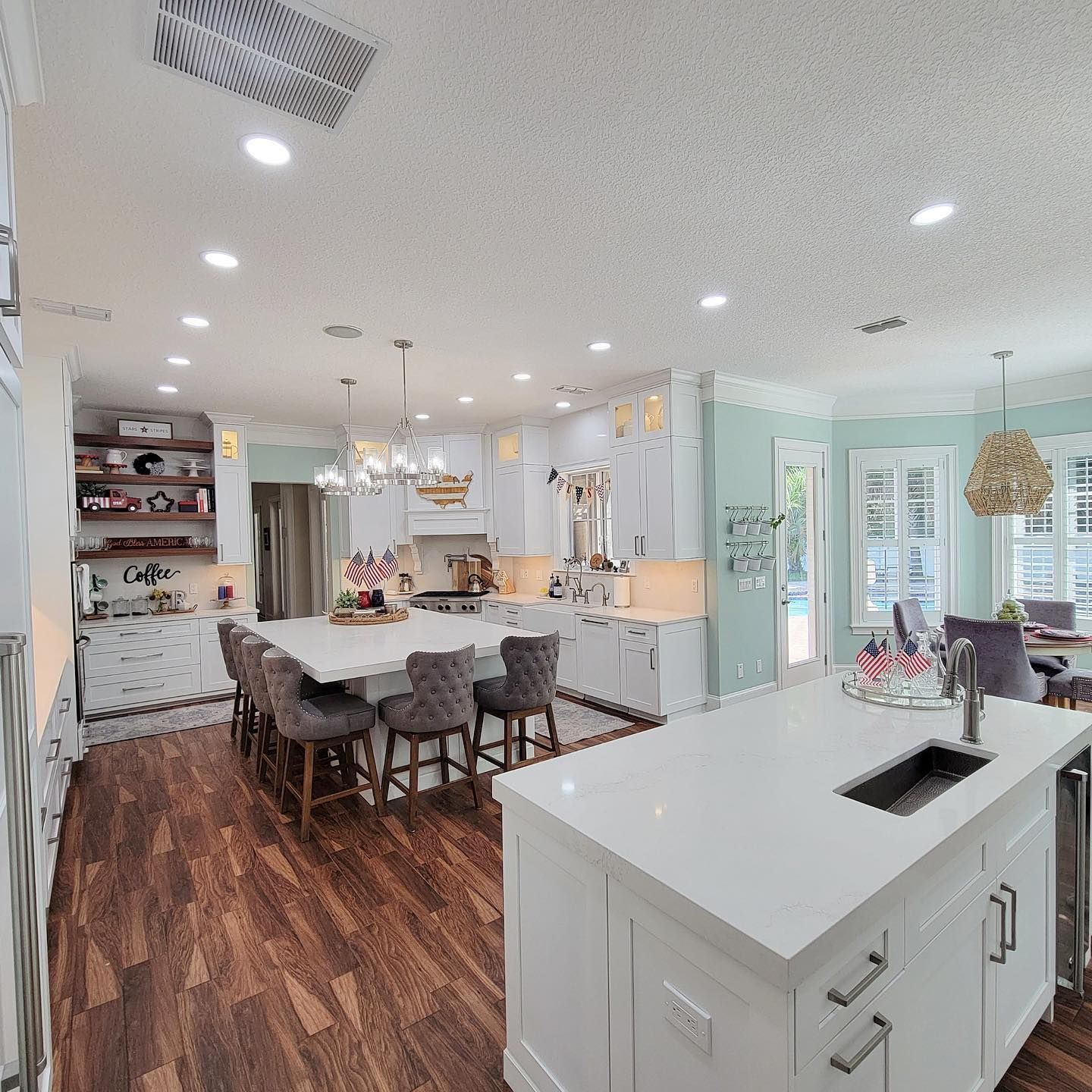 Spacious kitchen with white cabinets, island with seating, wooden floors, and a light blue accent wall.