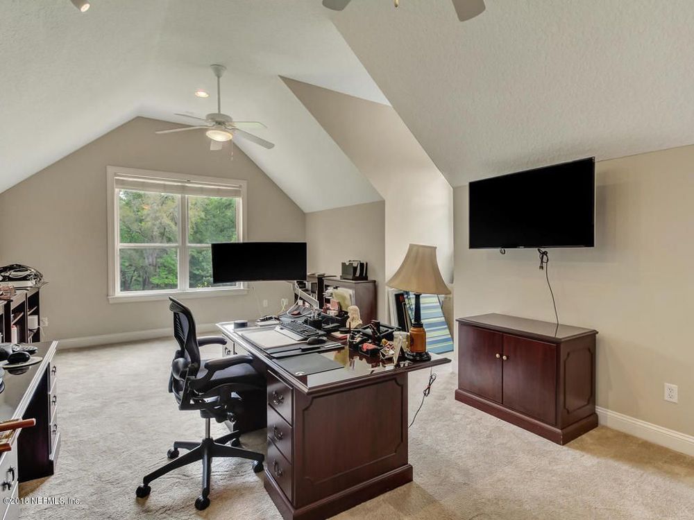 Home office with desk, dual monitors, TV, and window in attic space.