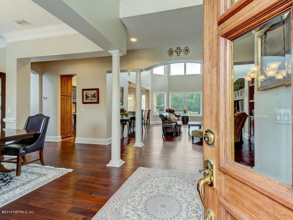 Open wooden front door, looking into a spacious home with hardwood floors, columns, and large windows.