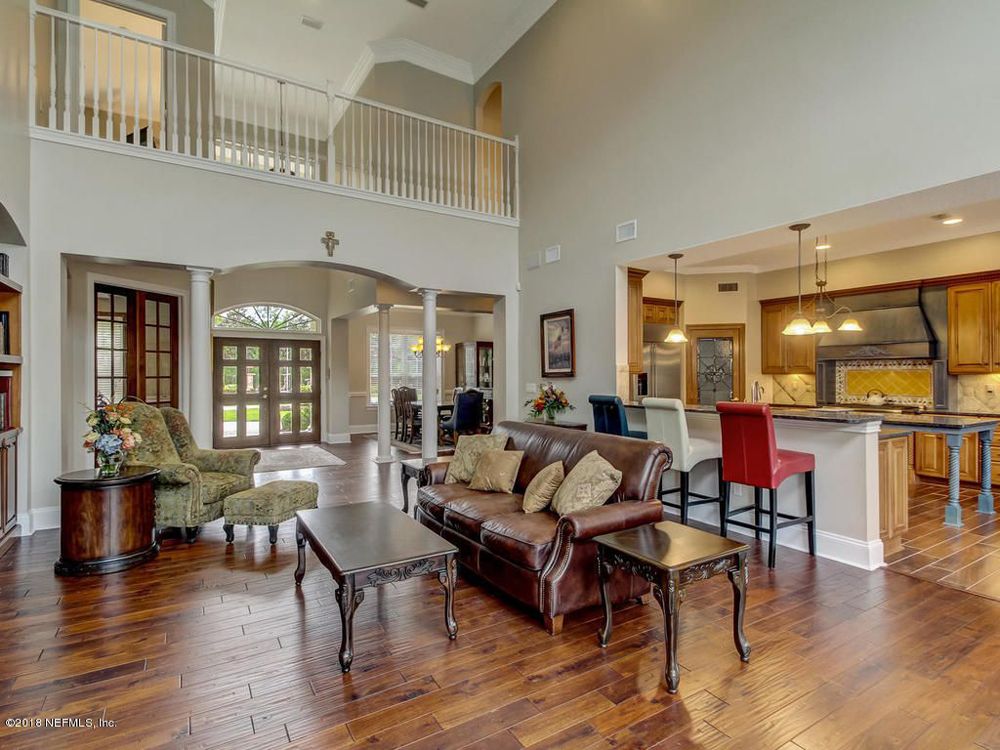 Spacious living room with brown leather sofa, kitchen bar, and upper-level balcony.