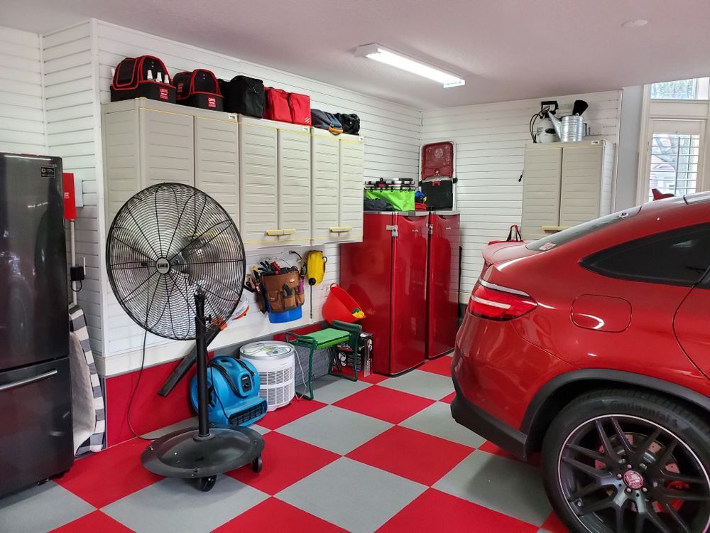 Red sports car parked in a red and gray checkered floor garage with storage cabinets and equipment.