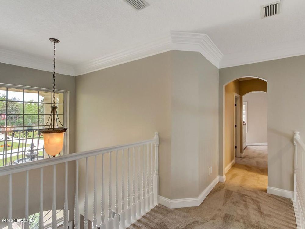 Hallway with beige walls, carpet, and white railing, with an arched doorway leading further inside.