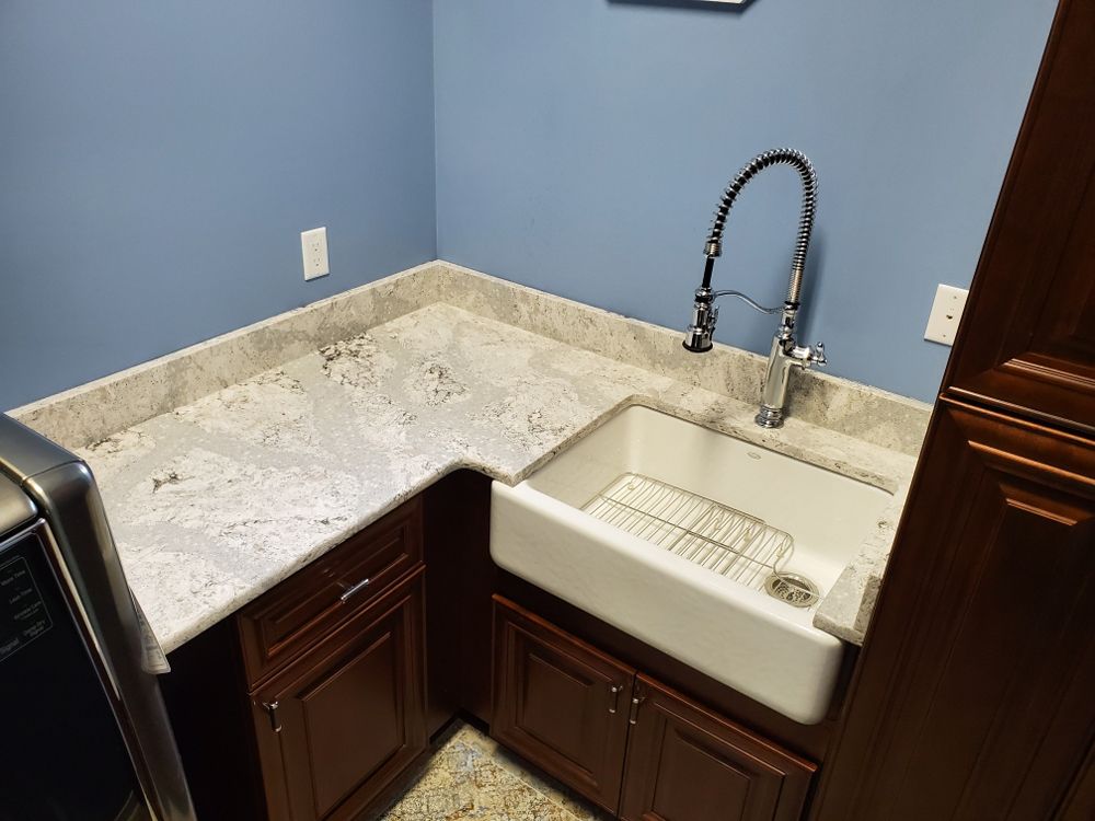 Laundry room with white farmhouse sink, granite countertop, blue walls, and dark cabinets.
